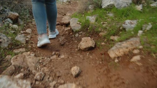 Weibliche Beine in Turnschuhen, die auf einem schmalen felsigen Pfad neben Bäumen den Berg hinuntersteigen.