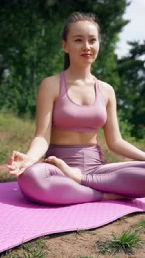 Vertical of Smiling Woman Meditates on Mat in Lotus Pose on Meadow