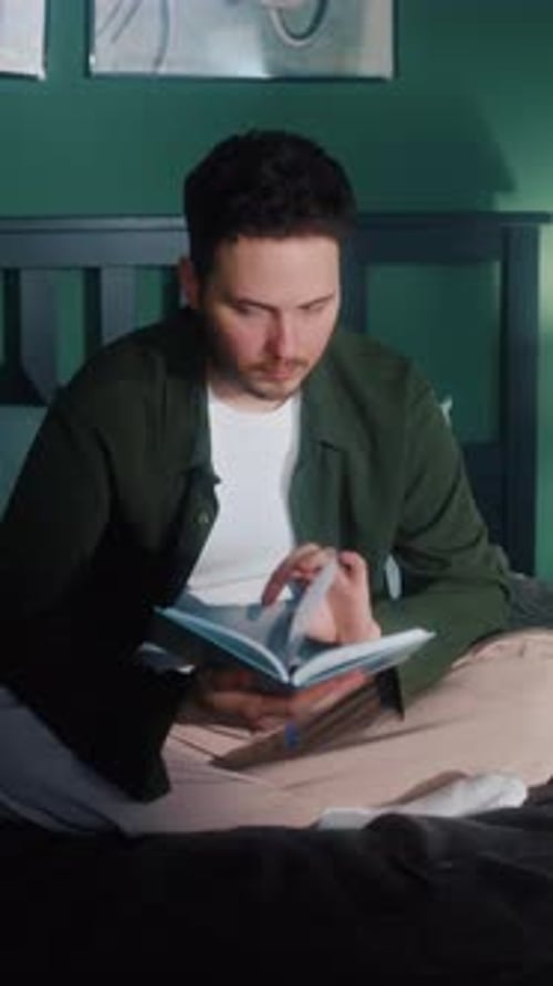 Man Reading Book While Sitting on Bed Indoors