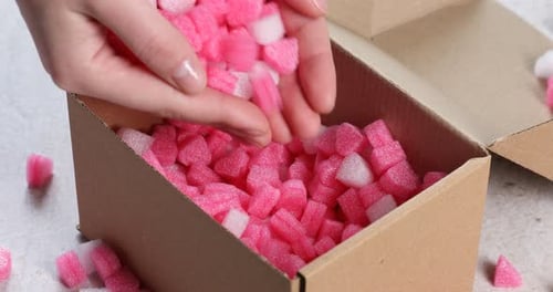 Femme mettant des morceaux de polystyrène dans une boîte en carton à une table gris clair, gros plan