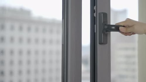 Young woman hand opening and closing modern plastic window by turning the handle to ventilate the ro