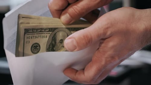 Hands Stuffing Cash into Envelope Financial Concept
