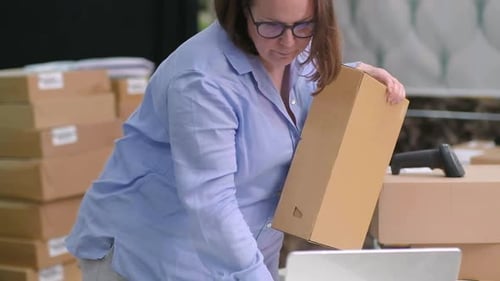 Woman Holding Box at Desk with Laptop