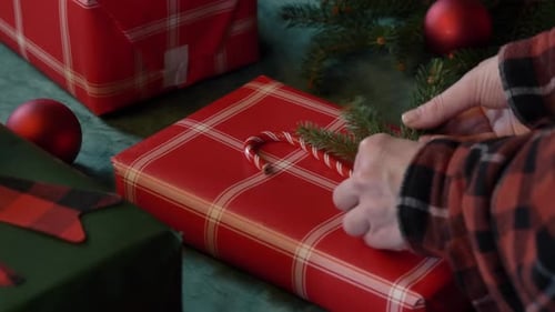 woman wrapping Christmas gifts on a table, with red boxes and a green tablecloth