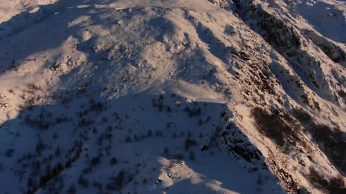 Panorama of a Snowy Mountain Range with Steep Cliffs and Shrubs Aerial View