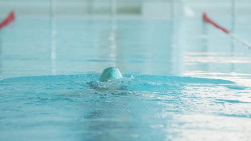 A Young Woman in Blue Swimsuit and Turquoise Swimming Cap Swims with a Breaststroke in the Pool