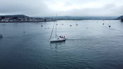 Sailing boat aerial view leaving Conwy seaside town harbour estuary to navigate quiet river