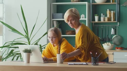 Woman Helping Child Use Laptop in Kitchen