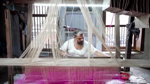 Indian mature man sitting at handloom weaving with purple thread