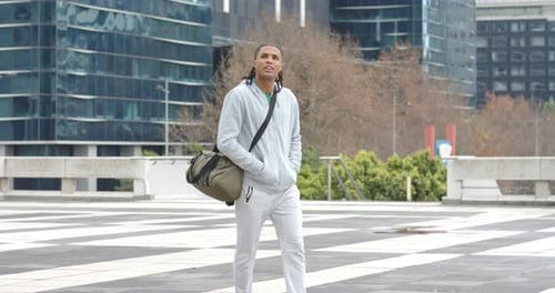Man entering plaza carrying duffle bag and scanning surroundings by glass high-rise buildings