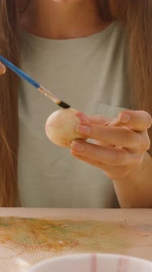Vertical video. Focused woman adding fine details to a pastel-colored Easter egg, demonstrating