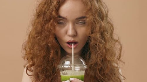 A Young Woman Enjoys a Refreshing Green Smoothie Indoors During the Afternoon