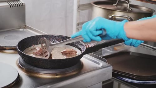 Chef in Restaurant Kitchen Stirs and Turns Meat