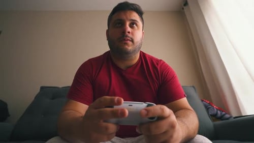 Young Adult Plays Video Game at Home on Couch