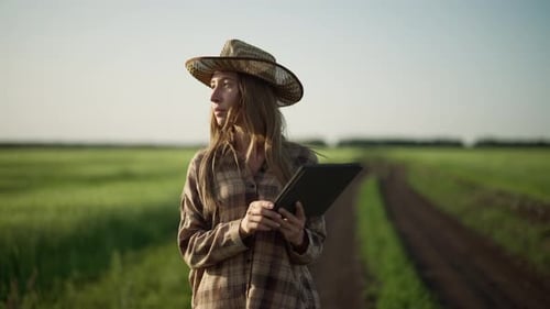 Farm Worker Woman with Tablet in Hands Walks on Agricultural Field Early Spring at Sunset Blonde
