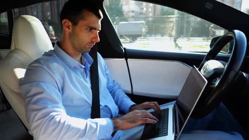 Handsome Entrepreneur Working on Notebook While Riding an Autonomous Self Driving Electric Car at