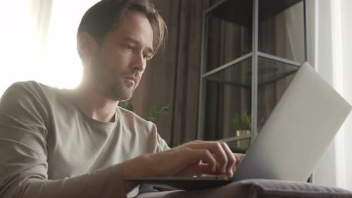 Man Works on Laptop on Couch Indoors