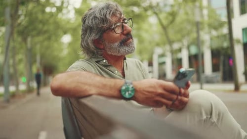 Man on Bench Uses Cell Phone in City Park