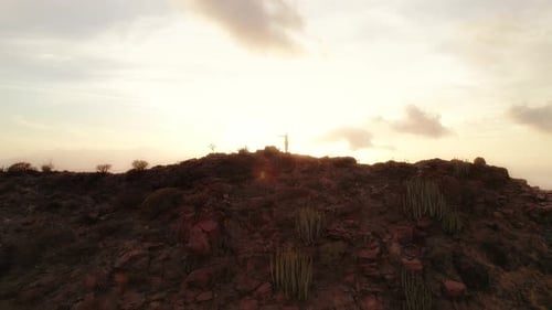 Person with arms outstretched standing on the peak of Los Gigantes Cliffs during sunset with a drama