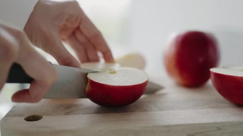 Nahaufnahme von Händen, die frischen roten Apfel auf einem Holzschneidebrett schneiden