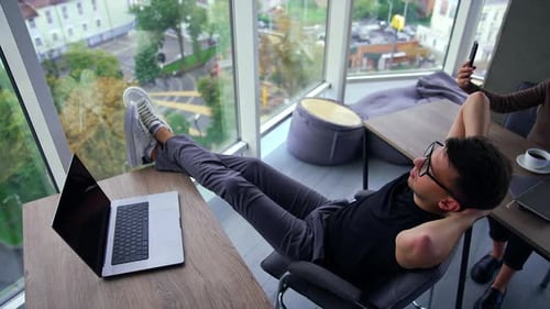 Relaxation from work in the office. Man sitting on the chair with legs on the desk.