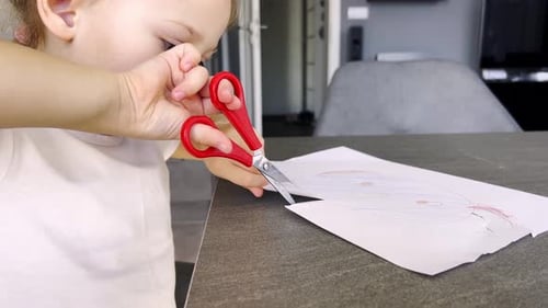 Child Cutting Drawing with Scissors at Table