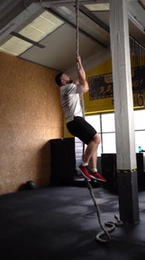 Muscular man performing rope climbing exercise during a functional training workout in slow motion
