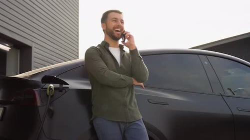 Handsome Man Phoning While Charging Car at Electric Vehicle Charging Station