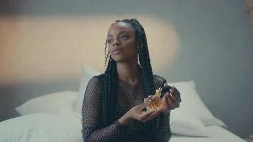 Front view of a smiling dark skinned girl applying perfume on her neck.