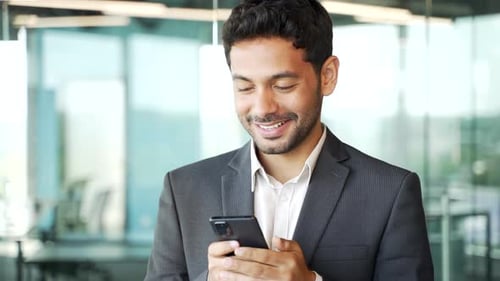 Close up. Young businessman in formal suit is using smartphone standing in business office. Handsome