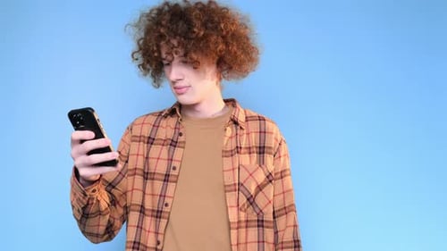 Cute Young Happy Student on Blue Background Looking at Phone