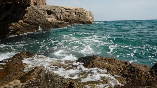 Espumosas olas de agua turquesa chocan contra las rocas a lo largo de la costa en Cámara lenta.