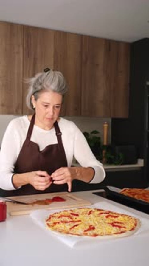Mature woman cooking homemade pizza in the kitchen