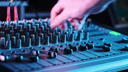 Male Hand Adjusting Faders Up And Down on Audio Mixer in Neon Light CloseUp