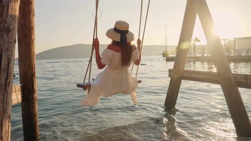 Slow motion of elegant woman in long dress enjoying swinging on swing and looking on the sunset
