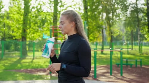 Woman Drinking Water After Exercising in Park