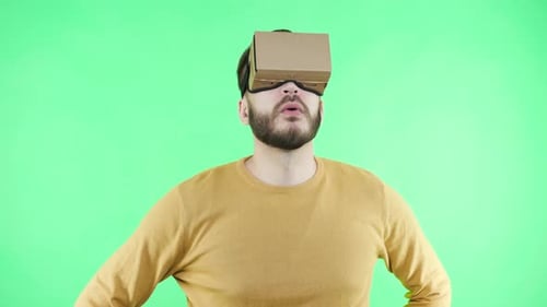 Man in vr glasses plays games on green screen background looking scared and surprised