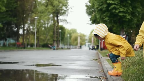 Boy jumps into puddle. Two kids in yellow waterproof cloak and boots playing outdoors after the rain