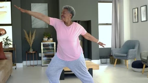 Mulher afro-americana sênior adotando uma postura ampla, estendendo os braços, melhorando o equilíbrio em casa