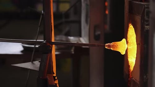 A glass blower pulling a glass cup from a high-powered furnace.