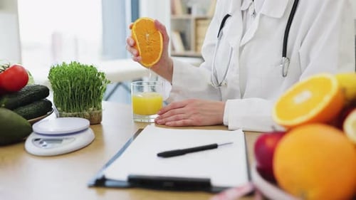 Woman in Lab Coat Holding Orange in Doctor's Office