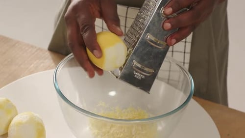 Mid adult male holding peeled lemon, using grater, grating zest into glass bowl at kitchen counter