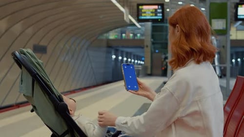Woman waits for subway while using smartphone with blue screen at station