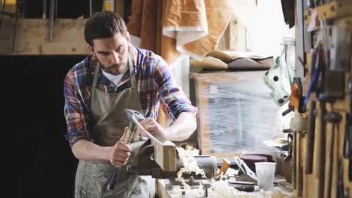 Man Carving Wood with Chisel in Workshop