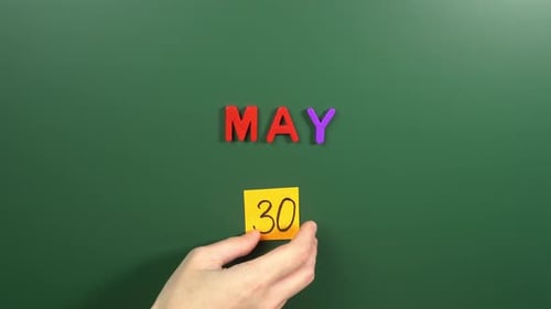 Hand sticking a sticker 30 May calendar day on school board. 30 date of May. Thirtieth day May