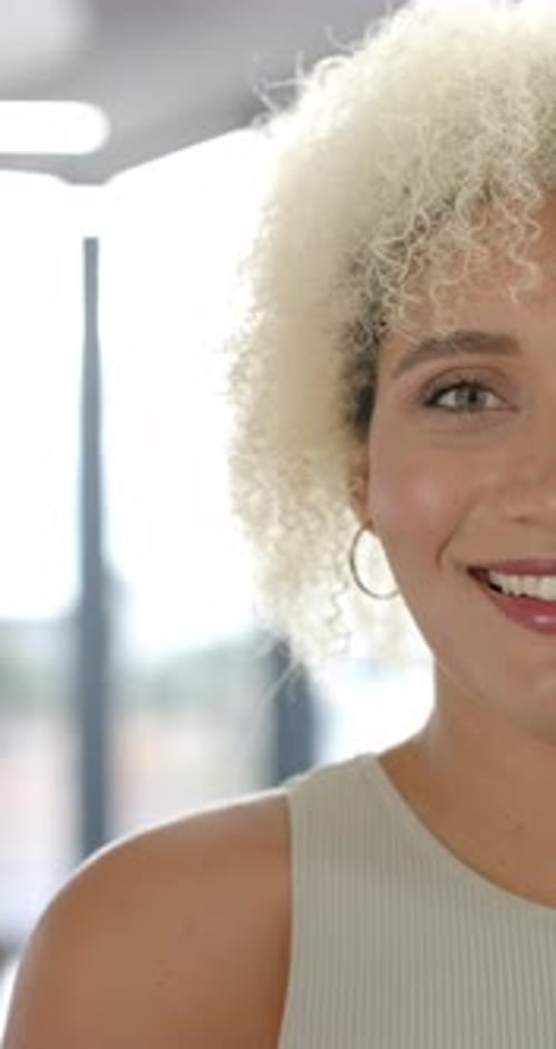Vidéo verticale : Femme souriante aux cheveux bouclés regardant la caméra dans un bureau lumineux