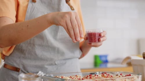 Woman Sprinkling Red Topping on Cinnamon Rolls at Home