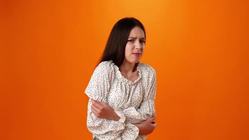 Teen Girl Suffering Stomach Ache Against Orange Background in Studio