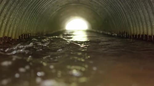 Hochwasser fließt durch ein Wellrohr mit Licht am Ende, Zoom-Aufnahme