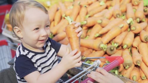 Smiling little boy chooses fresh carrot in grocery store